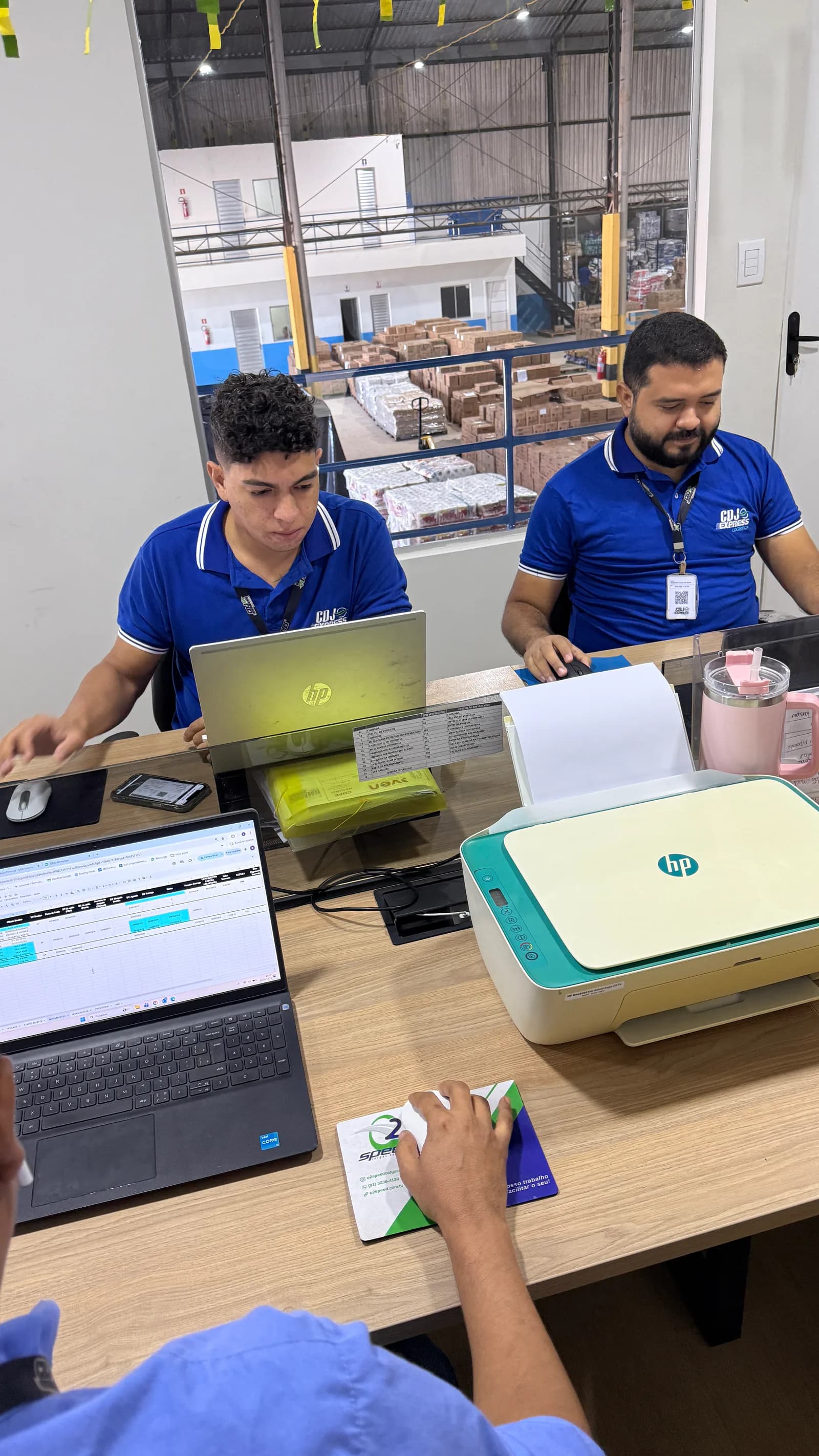 Profissionais da CDJ Express acompanhando a operação em computadores diante do galpão
